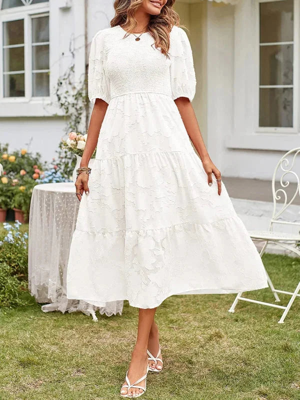 White midi dress with floral textured patterns and tiered design by Klaire. Made of lightweight and breathable fabric.