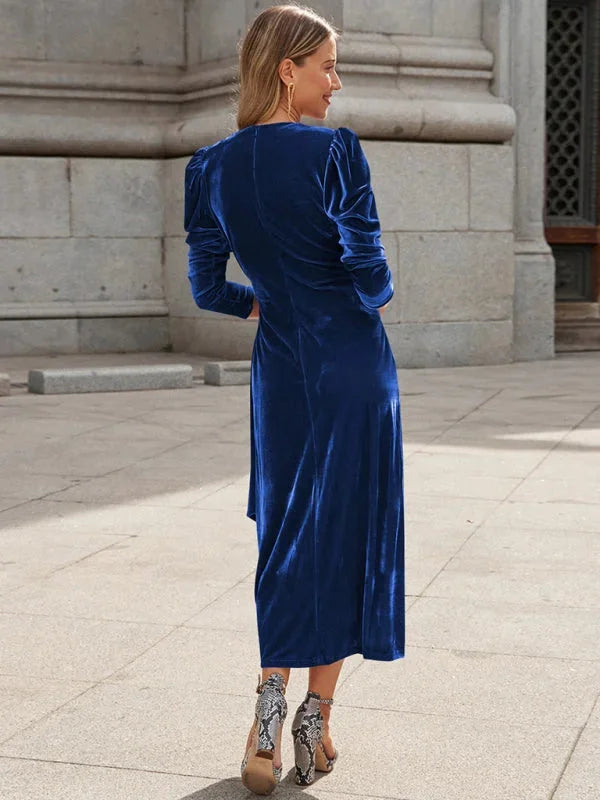 Black velvet wrap dress with puffed sleeves on model standing against a white background.