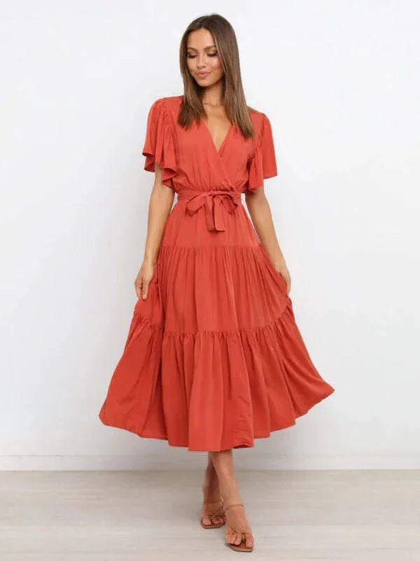 Orange tiered midi dress made of flowing fabric with a belt, perfect for daywear or special occasions.